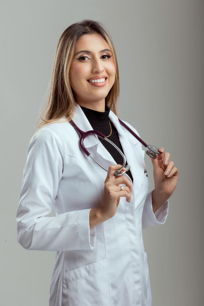 Dra. Juliana Rodrigues sorrindo, de jaleco branco, segurando o estetoscópio